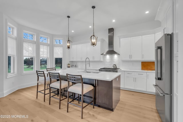 kitchen featuring a center island with sink, sink, wall chimney exhaust hood, high quality fridge, and white cabinetry