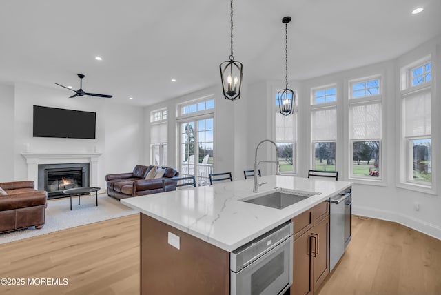 kitchen with sink, hanging light fixtures, light stone counters, an island with sink, and light hardwood / wood-style floors