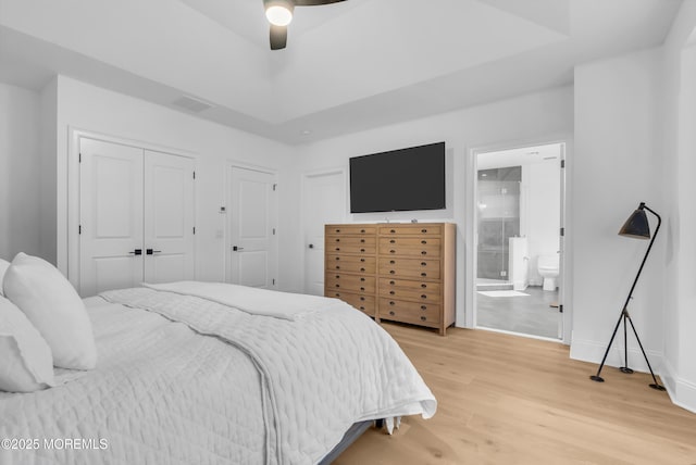 bedroom featuring a raised ceiling, connected bathroom, ceiling fan, and hardwood / wood-style floors