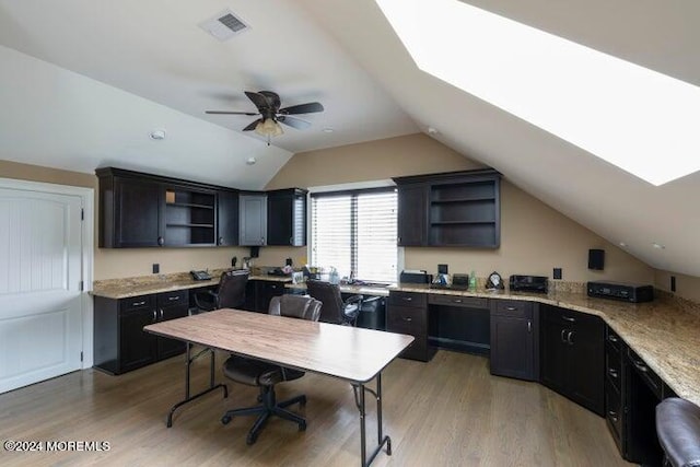 kitchen with lofted ceiling with skylight, light hardwood / wood-style flooring, light stone countertops, and ceiling fan