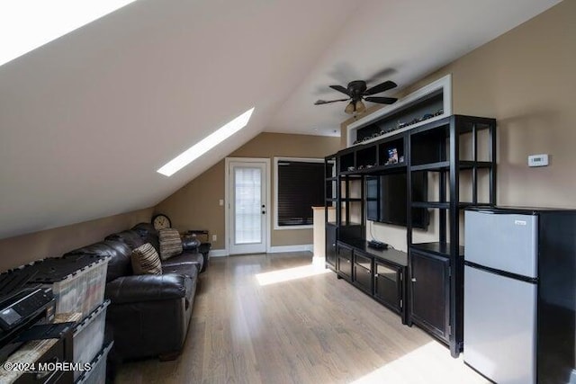 living room featuring ceiling fan, vaulted ceiling with skylight, and light hardwood / wood-style flooring