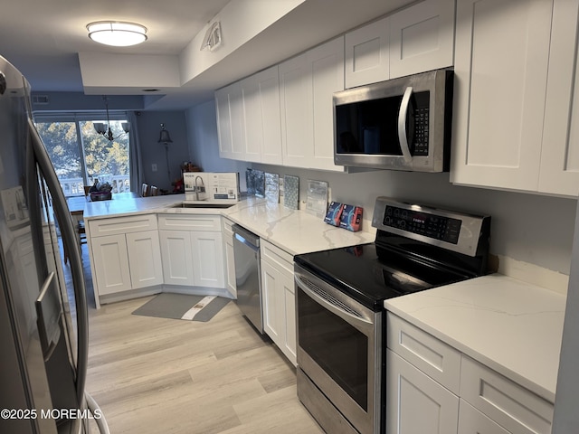 kitchen with sink, appliances with stainless steel finishes, kitchen peninsula, light stone countertops, and white cabinets