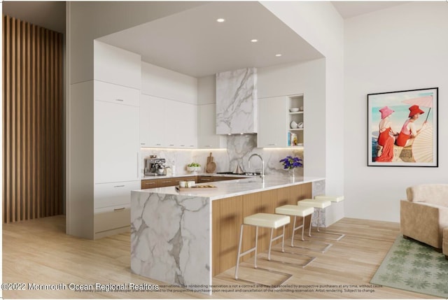 kitchen with light stone counters, a breakfast bar, light hardwood / wood-style flooring, backsplash, and white cabinetry