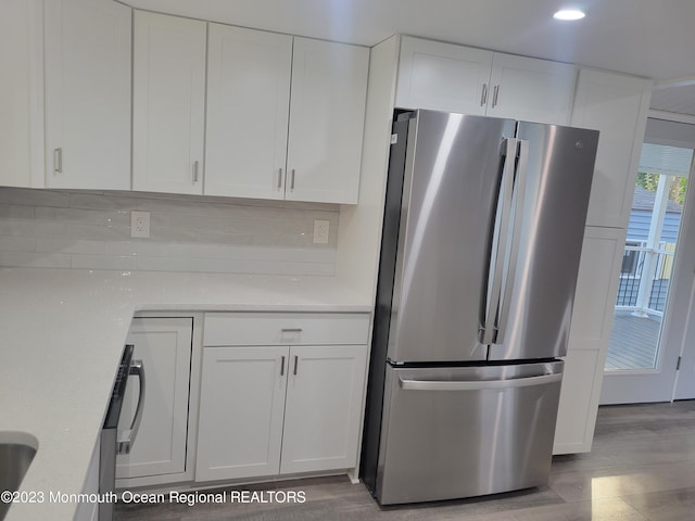 kitchen featuring white cabinetry, light stone countertops, stainless steel fridge, hardwood / wood-style floors, and tasteful backsplash