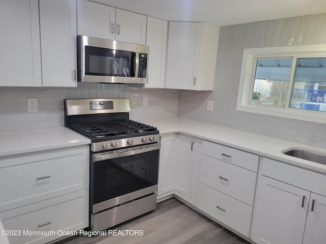 kitchen with white cabinets, appliances with stainless steel finishes, tasteful backsplash, and light hardwood / wood-style flooring