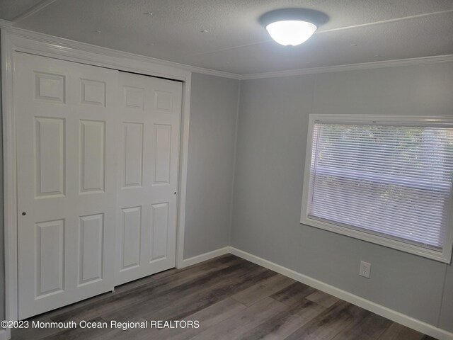 unfurnished bedroom with dark wood-type flooring, a closet, a textured ceiling, and ornamental molding