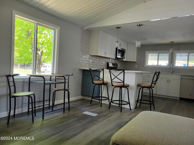 kitchen with a breakfast bar area, appliances with stainless steel finishes, white cabinetry, and lofted ceiling