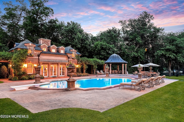 pool at dusk featuring a gazebo, a yard, a patio, a diving board, and french doors