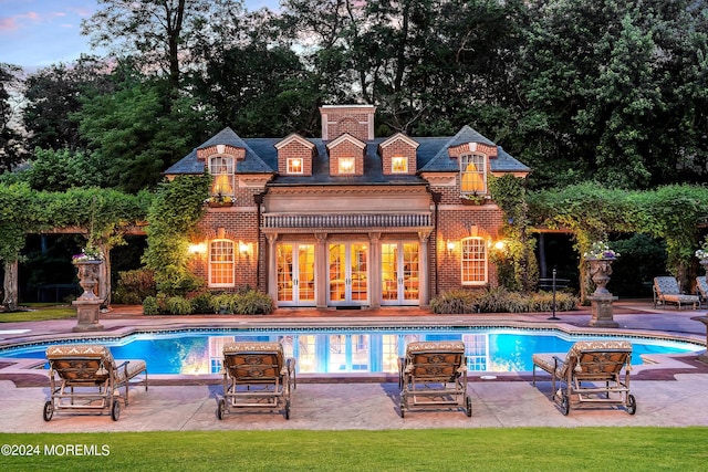 pool at dusk with french doors and a patio area