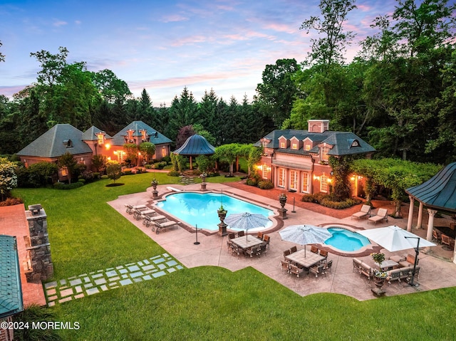 pool at dusk featuring an outbuilding, a patio, and a lawn