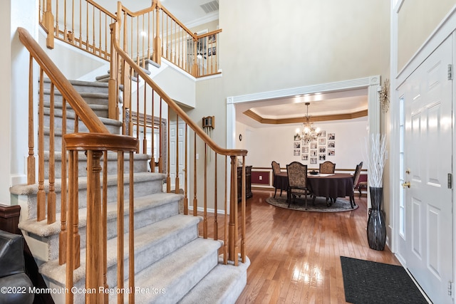 entrance foyer featuring a raised ceiling, a towering ceiling, a notable chandelier, and light wood-type flooring