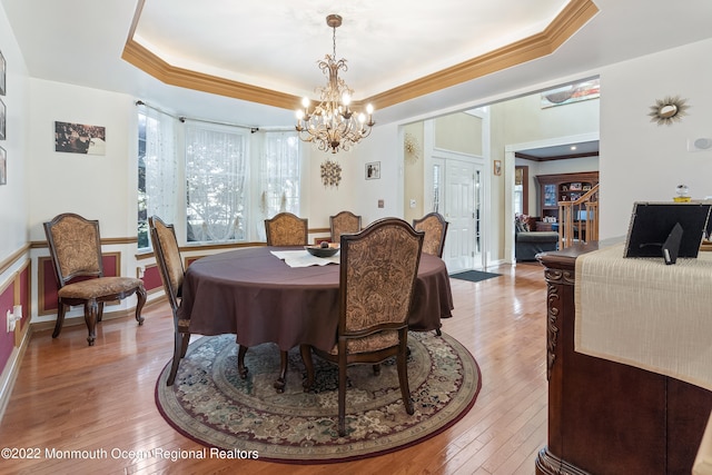 dining space with crown molding, an inviting chandelier, light hardwood / wood-style floors, and a tray ceiling