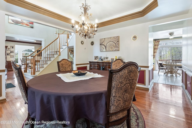 dining room featuring a raised ceiling, light hardwood / wood-style floors, ceiling fan with notable chandelier, and crown molding