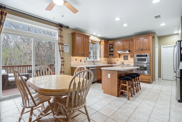 kitchen featuring light tile floors, a center island, ceiling fan, appliances with stainless steel finishes, and backsplash