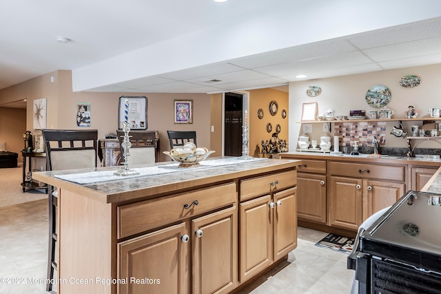 kitchen featuring a drop ceiling, a kitchen island, light tile floors, a kitchen breakfast bar, and stove