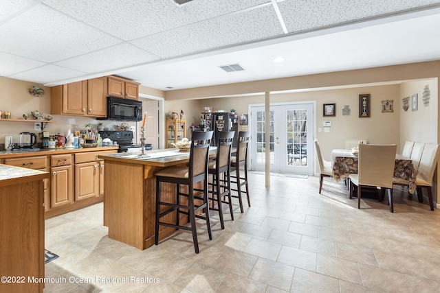 kitchen with black appliances, a paneled ceiling, a center island with sink, french doors, and a breakfast bar area