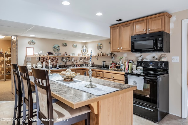 kitchen featuring a breakfast bar, a drop ceiling, light colored carpet, and black appliances