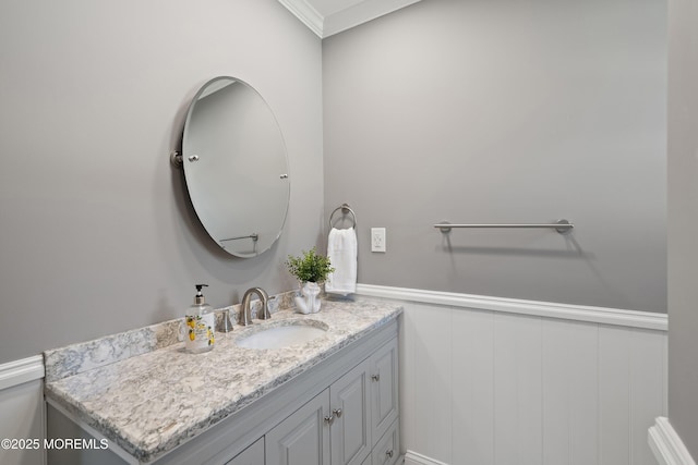 bathroom with crown molding, a wainscoted wall, vanity, and a decorative wall
