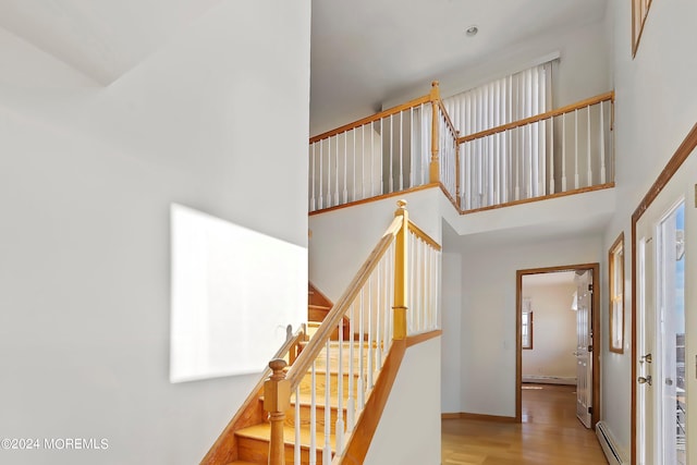 stairs featuring a towering ceiling, a baseboard radiator, and light wood-type flooring