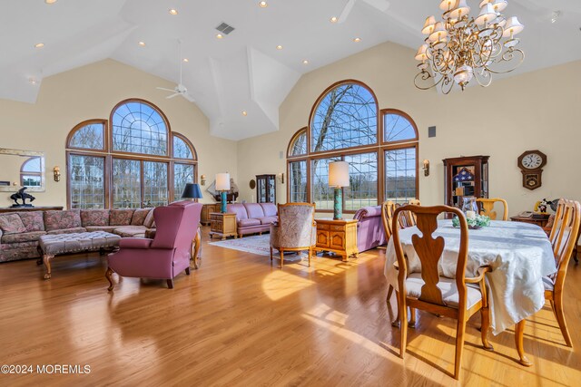 dining room with ceiling fan with notable chandelier, high vaulted ceiling, and light wood-type flooring