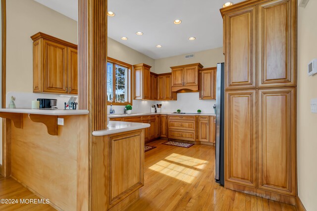 kitchen with kitchen peninsula, a kitchen breakfast bar, stainless steel refrigerator, light hardwood / wood-style flooring, and ornate columns