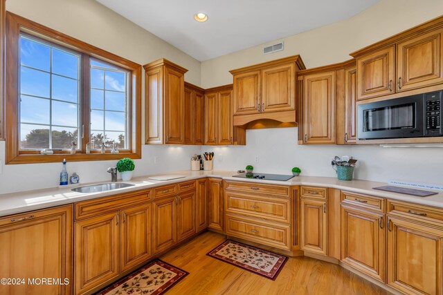 kitchen with light hardwood / wood-style flooring, black microwave, sink, electric cooktop, and premium range hood