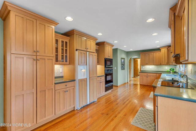 kitchen featuring light brown cabinetry, black appliances, light wood-type flooring, and tasteful backsplash