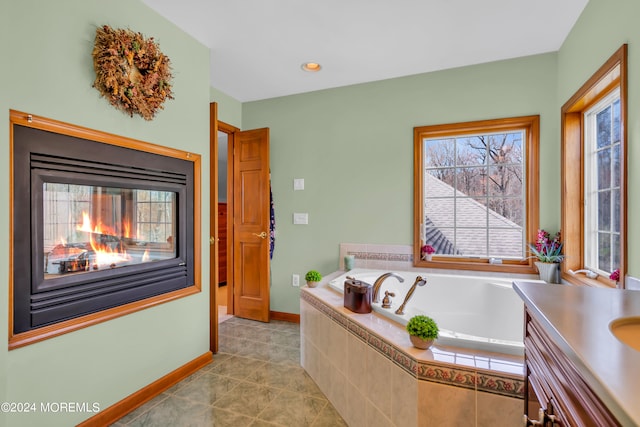 bathroom with vanity, a multi sided fireplace, a relaxing tiled tub, and tile patterned floors