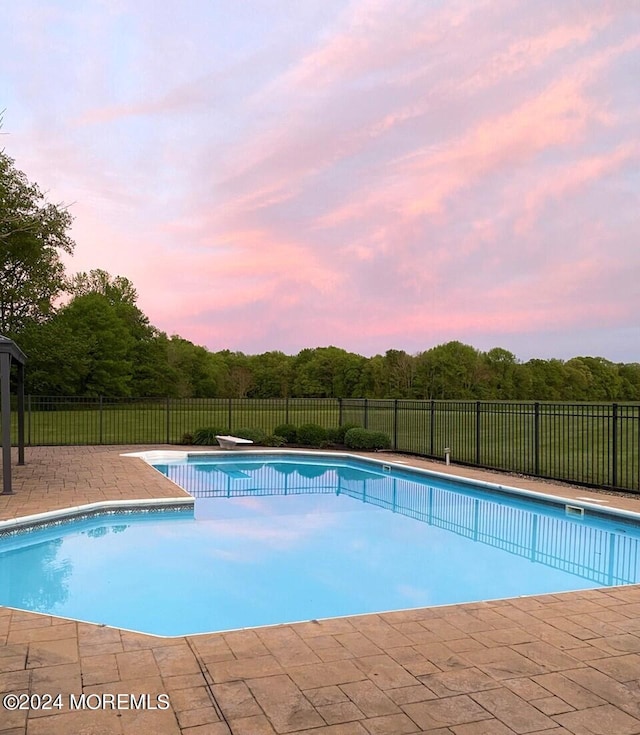 pool at dusk featuring a patio area and a diving board