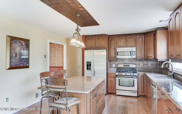 kitchen with a kitchen bar, sink, stainless steel appliances, pendant lighting, and light stone countertops