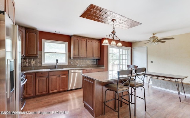 kitchen with hanging light fixtures, backsplash, stainless steel appliances, a center island, and light wood-type flooring