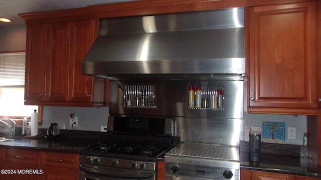 kitchen with dark stone counters, wall chimney exhaust hood, sink, and gas range