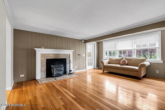 unfurnished living room with a wood stove, wooden walls, light hardwood / wood-style flooring, and ornamental molding