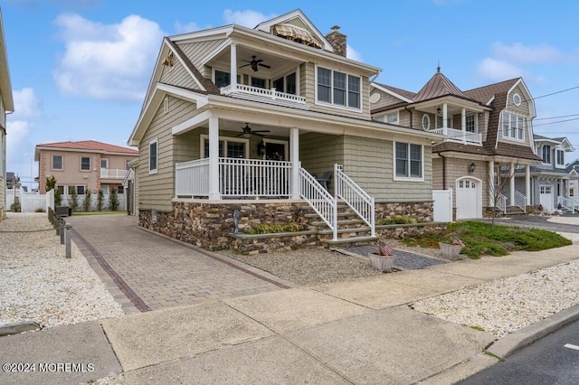 shingle-style home with a balcony, driveway, a porch, a chimney, and ceiling fan