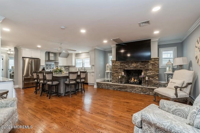 living room with visible vents, ceiling fan, ornamental molding, a stone fireplace, and wood finished floors