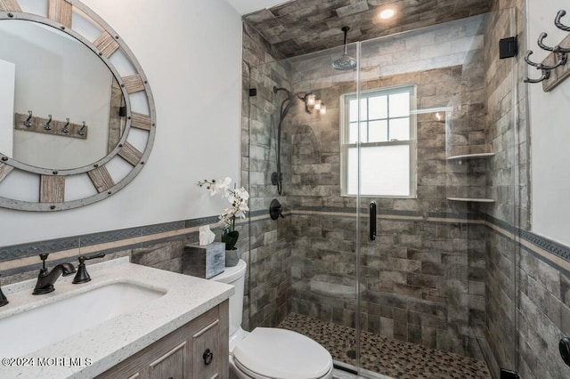 bathroom with toilet, a stall shower, tile walls, wainscoting, and vanity