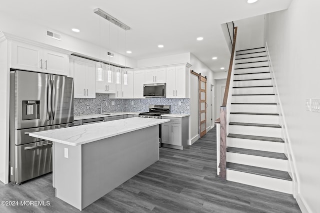 kitchen with a kitchen island, stainless steel appliances, a barn door, pendant lighting, and white cabinets