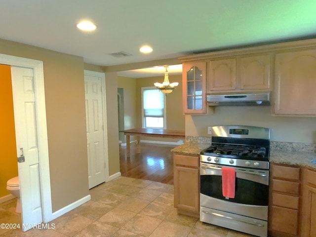 kitchen with light brown cabinetry, light tile patterned floors, an inviting chandelier, and stainless steel range with gas cooktop