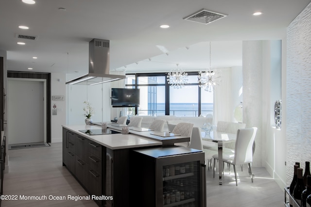 kitchen with wall chimney exhaust hood, a center island, pendant lighting, a water view, and a notable chandelier