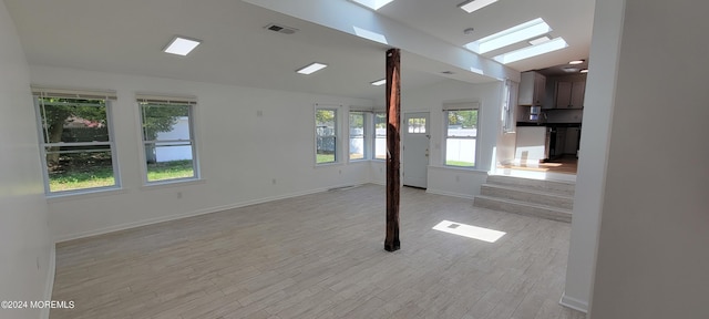 empty room with plenty of natural light, light hardwood / wood-style flooring, and vaulted ceiling with skylight