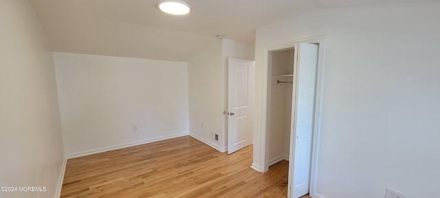 unfurnished bedroom with a closet, light hardwood / wood-style floors, and vaulted ceiling