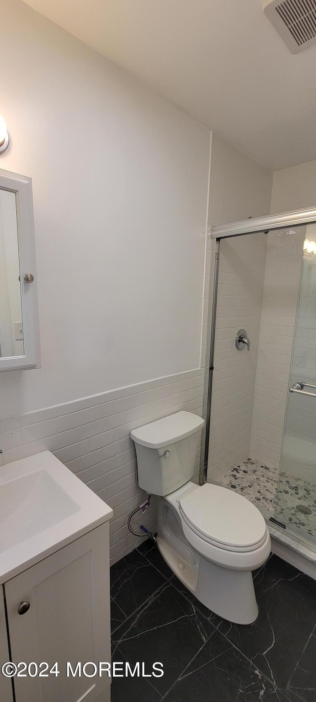 bathroom featuring tile flooring, tile walls, a shower with shower door, toilet, and vanity