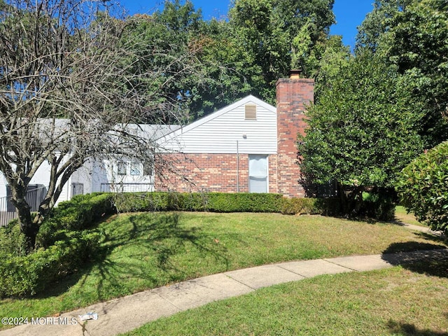 exterior space featuring brick siding, a lawn, and a chimney