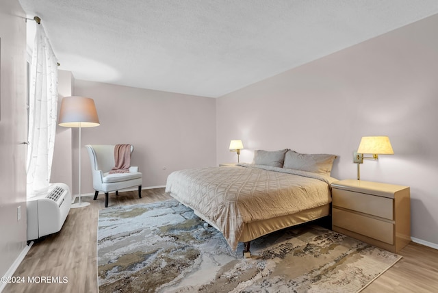 bedroom with a wall mounted air conditioner, hardwood / wood-style floors, and a textured ceiling