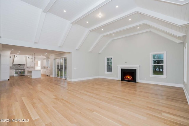 unfurnished living room with beamed ceiling, high vaulted ceiling, light hardwood / wood-style flooring, and a healthy amount of sunlight