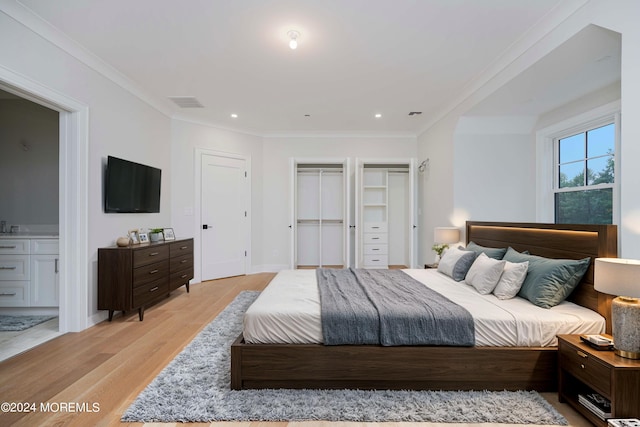 bedroom with ensuite bath, light wood-type flooring, two closets, and crown molding