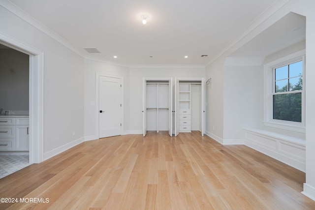 unfurnished bedroom featuring two closets, light hardwood / wood-style flooring, ensuite bath, and crown molding