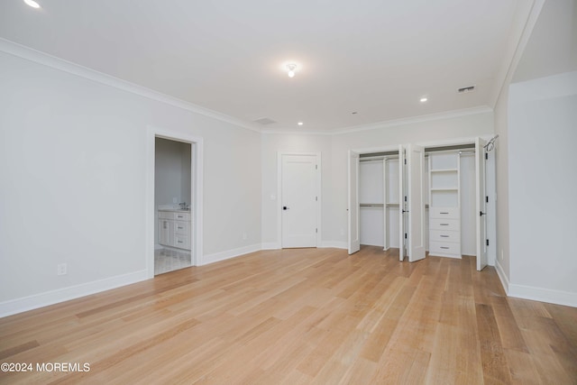 unfurnished bedroom featuring two closets, crown molding, light wood-type flooring, and ensuite bath