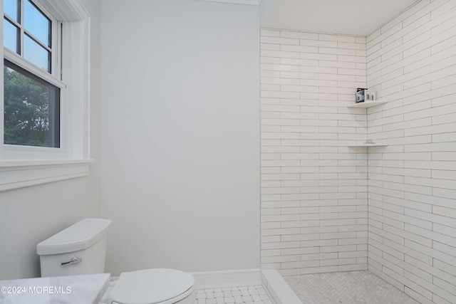 bathroom featuring a tile shower, tile patterned flooring, and toilet