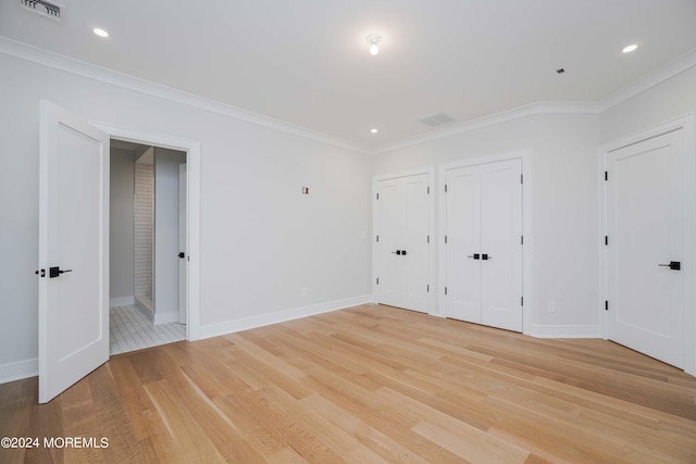 unfurnished bedroom featuring light hardwood / wood-style floors, connected bathroom, ornamental molding, and two closets